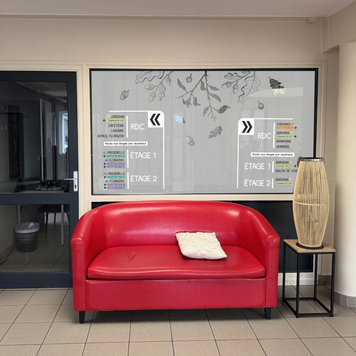 Vitrophanie de signalétique directionnelle sur cloison vitrée dans un hall d'accueil avec canapé rouge.