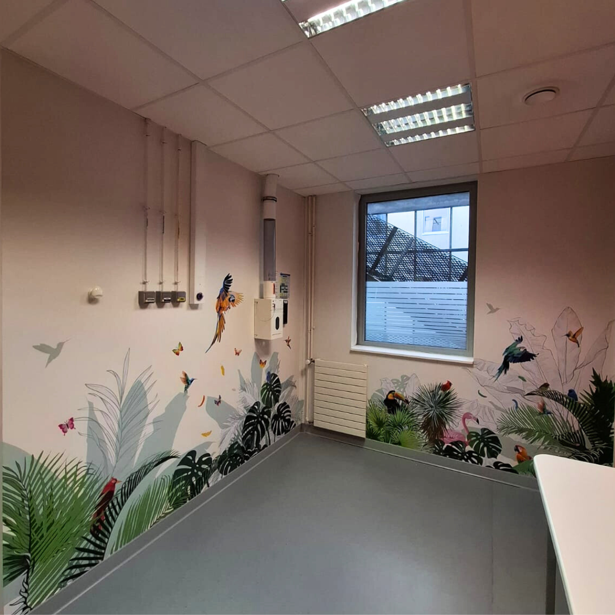 Décoration adhésive murale thématique jungle avec oiseaux tropicaux et feuillages exotiques dans une pièce de service.