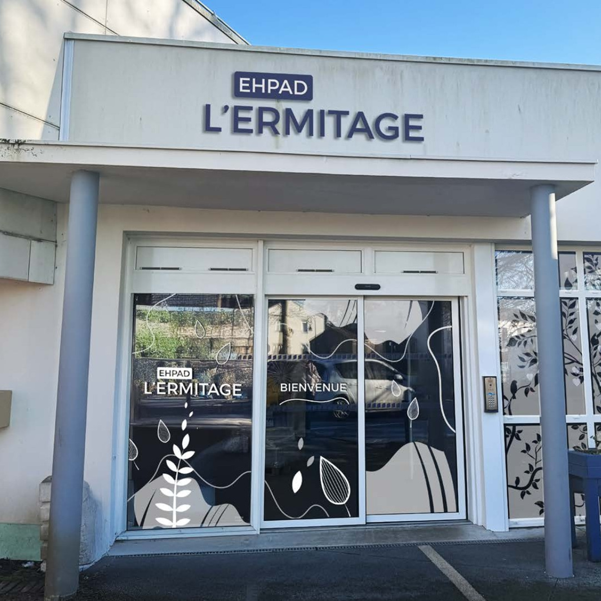 Vitrophanie décorative et enseigne de l'EHPAD L'Ermitage sur la façade d'entrée.