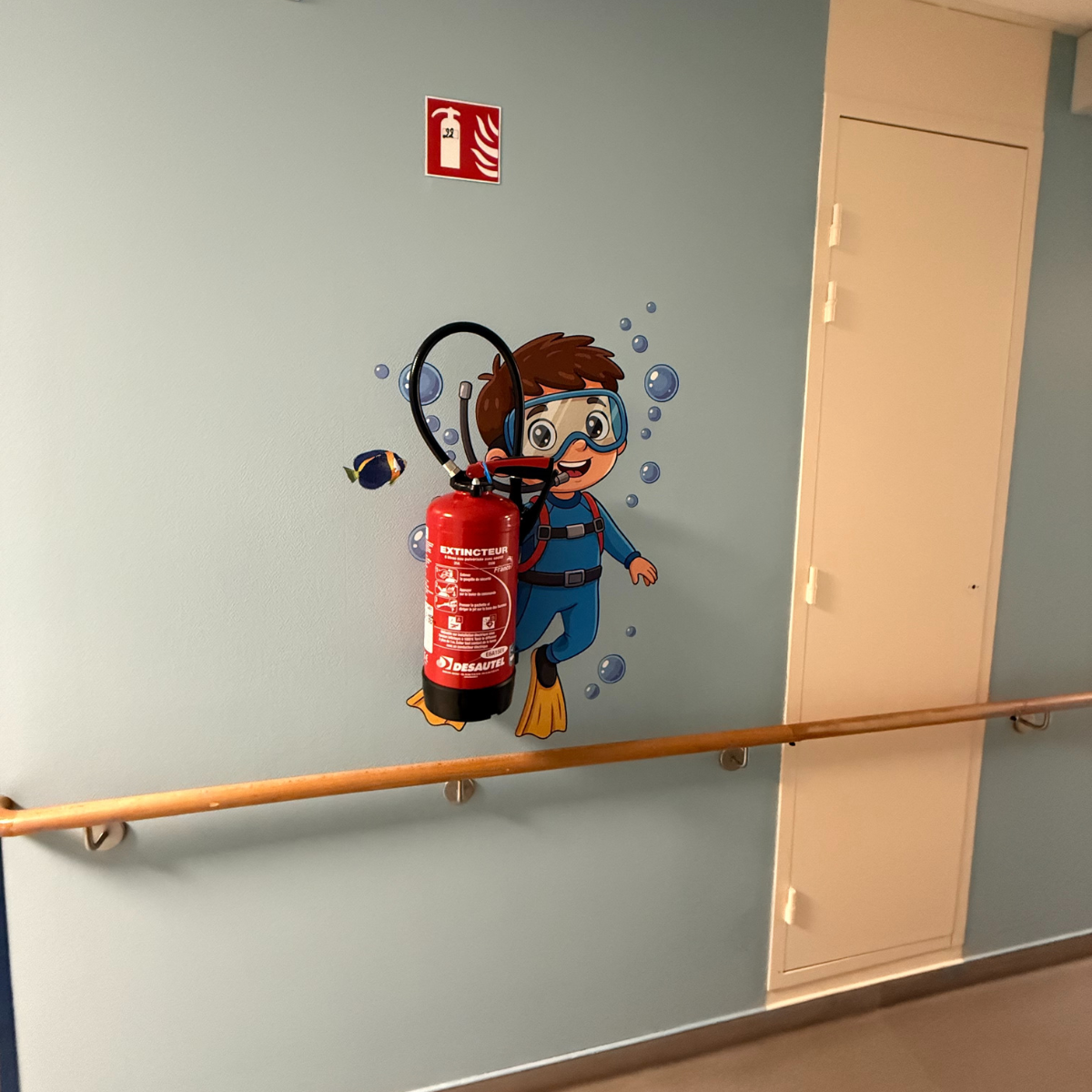 Décoration murale adhésive ludique avec un personnage de plongeur entourant un extincteur dans un couloir.