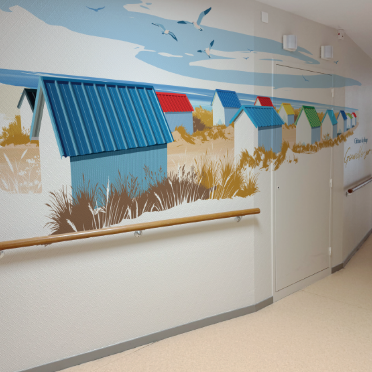 Décoration murale adhésive en couloir représentant des cabines de plage colorées et des mouettes.