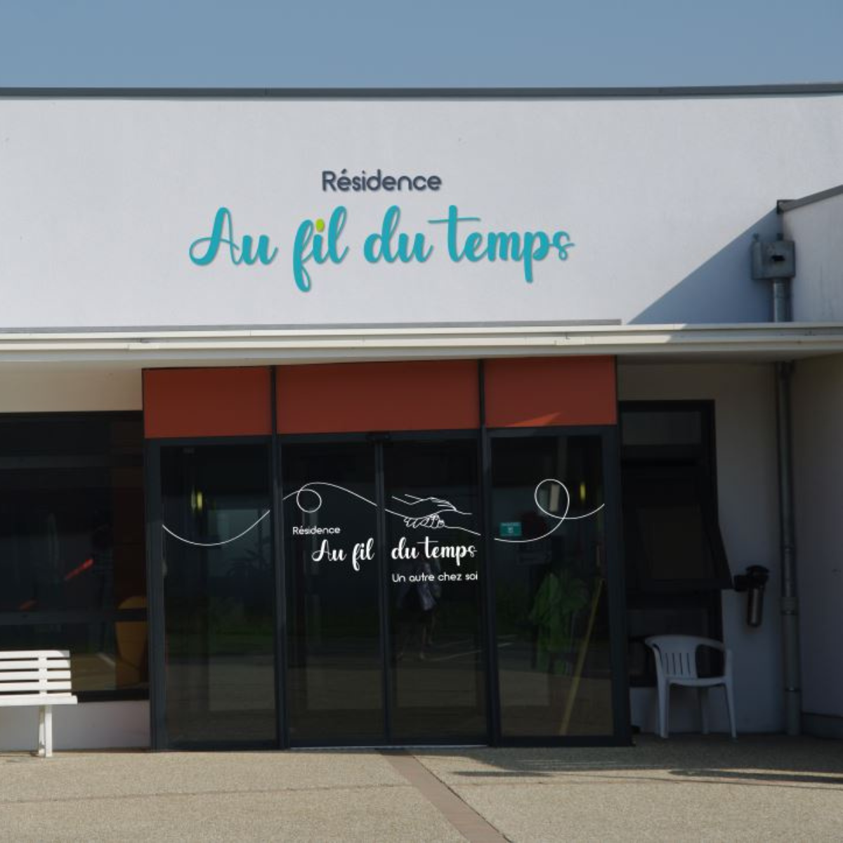 Entrée principale de la Résidence Au fil du temps avec enseigne murale bleue et vitrophanie sur les portes vitrées.