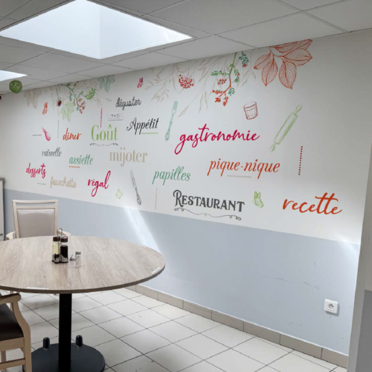 Décoration murale adhésive avec mots-clés de gastronomie française et illustrations de cuisine sur un mur de restaurant.